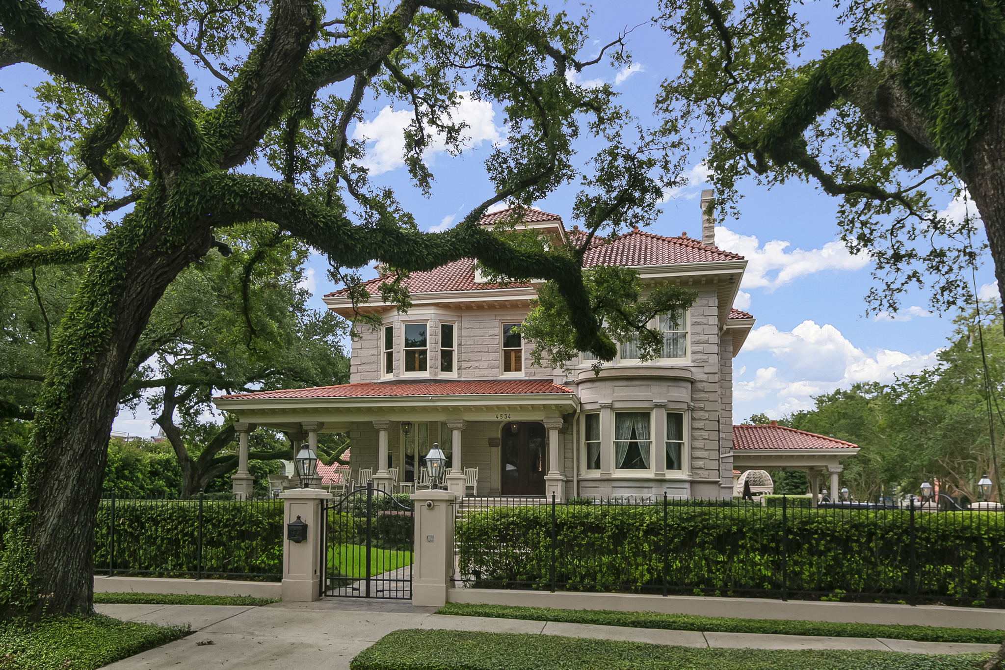A grand New Orleans home with a terracotta roof framed by sprawling live oaks in Lakeview